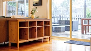 A wooden console table with a vase of flowers, a bench, and a view of a deck through glass doors. - New Melbourne Staycation 3BRM (Glen Waverley)