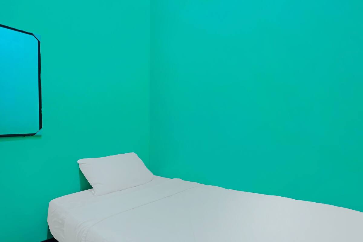 Une petite chambre avec un lit simple, un mur de couleur turquoise et une couvre-lit blanche.