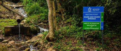 A sign for Ikogosi Warm Springs Resort with a natural waterfall and lush greenery.