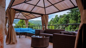 An outdoor seating area with wicker furniture and a blue sofa, overlooking a lush green landscape. - Ikogosi Warm Springs Resort and Conference Center (Ikogosi)