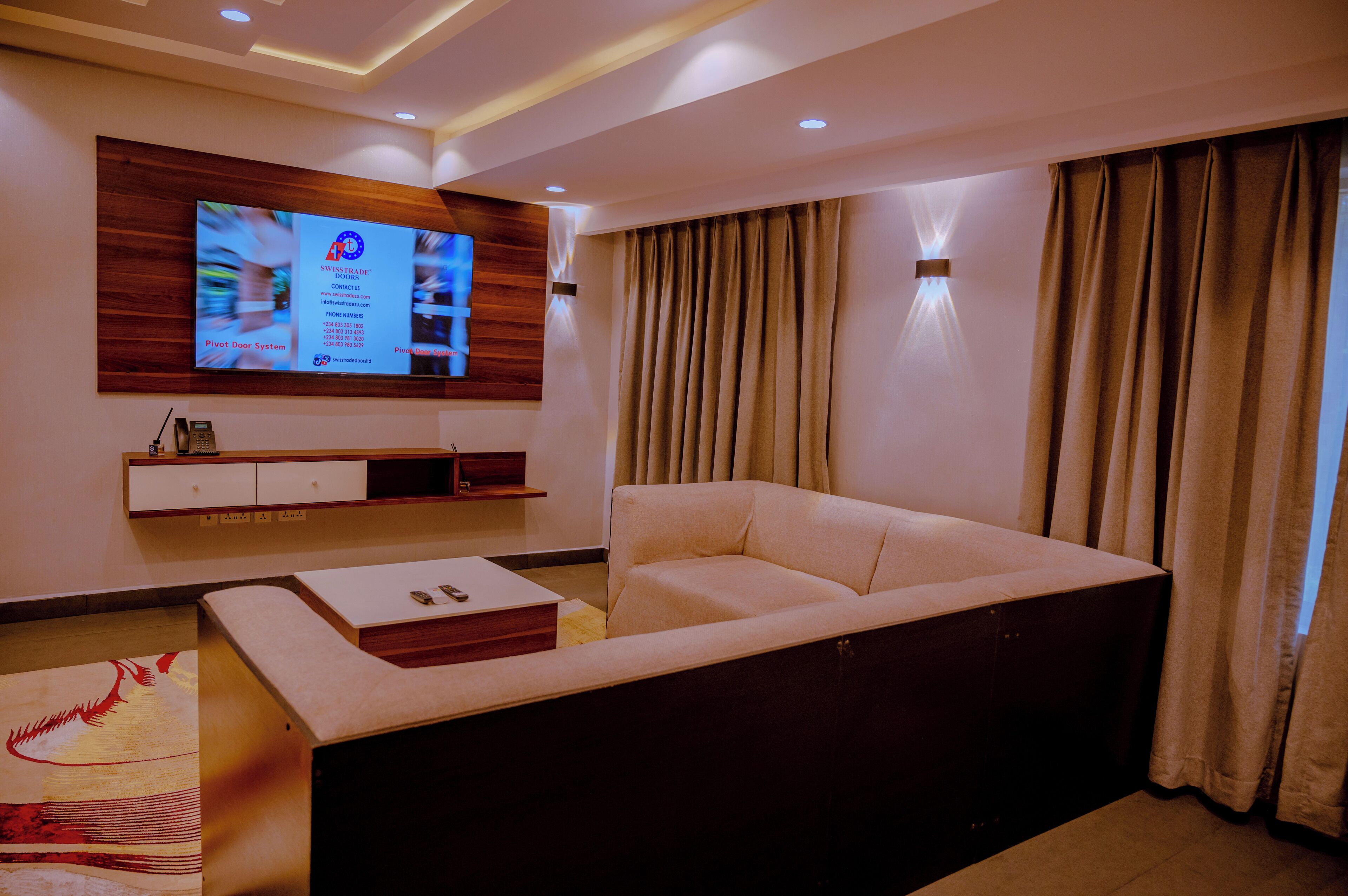 A modern living room with a flat-screen TV mounted on the wall, a beige sofa, and a wooden entertainment unit below.