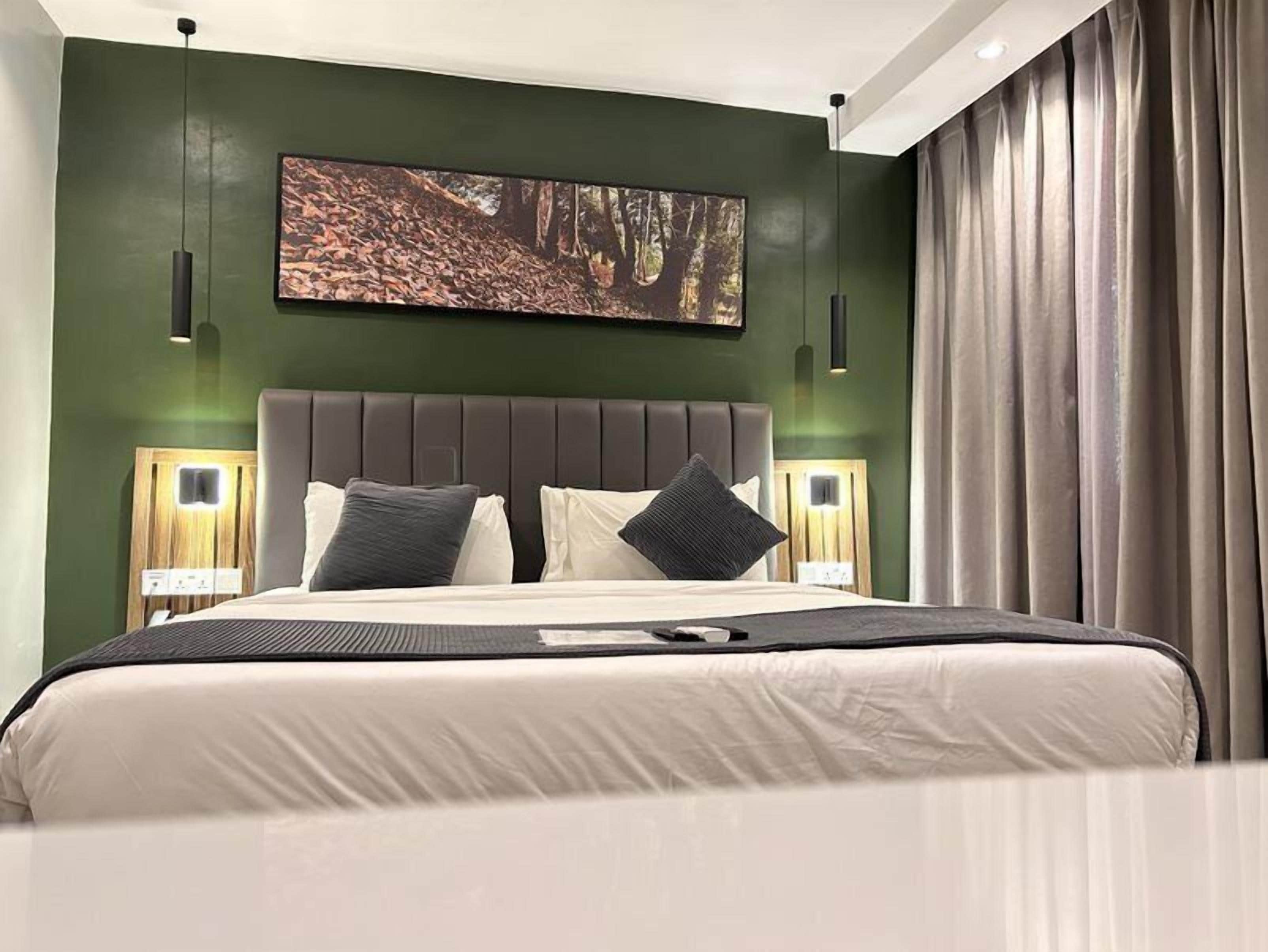 Een moderne slaapkamer met een groot bed, donkergroene muren en een kunstwerk met een boslandschap erboven.