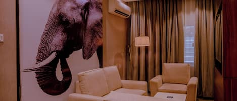 A room with a large elephant mural, two beige armchairs, a lamp, and a wooden wall.