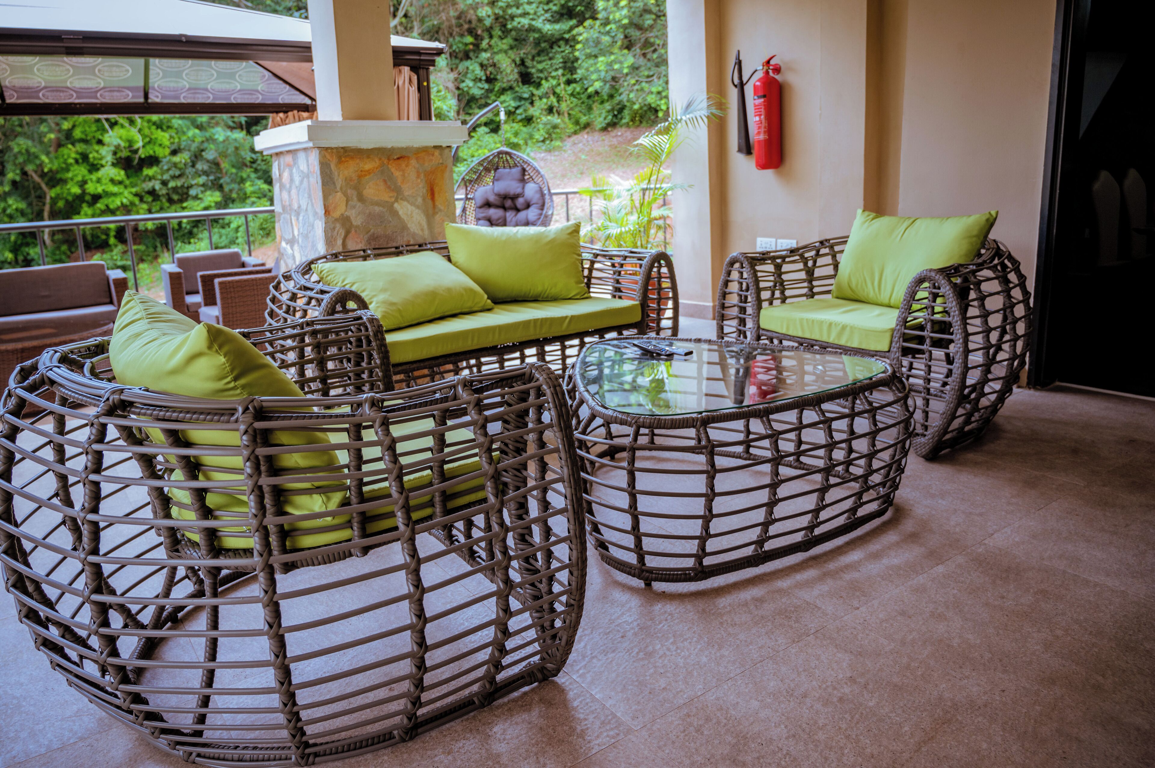 Wicker furniture with green cushions, a glass table, and a stone pillar.