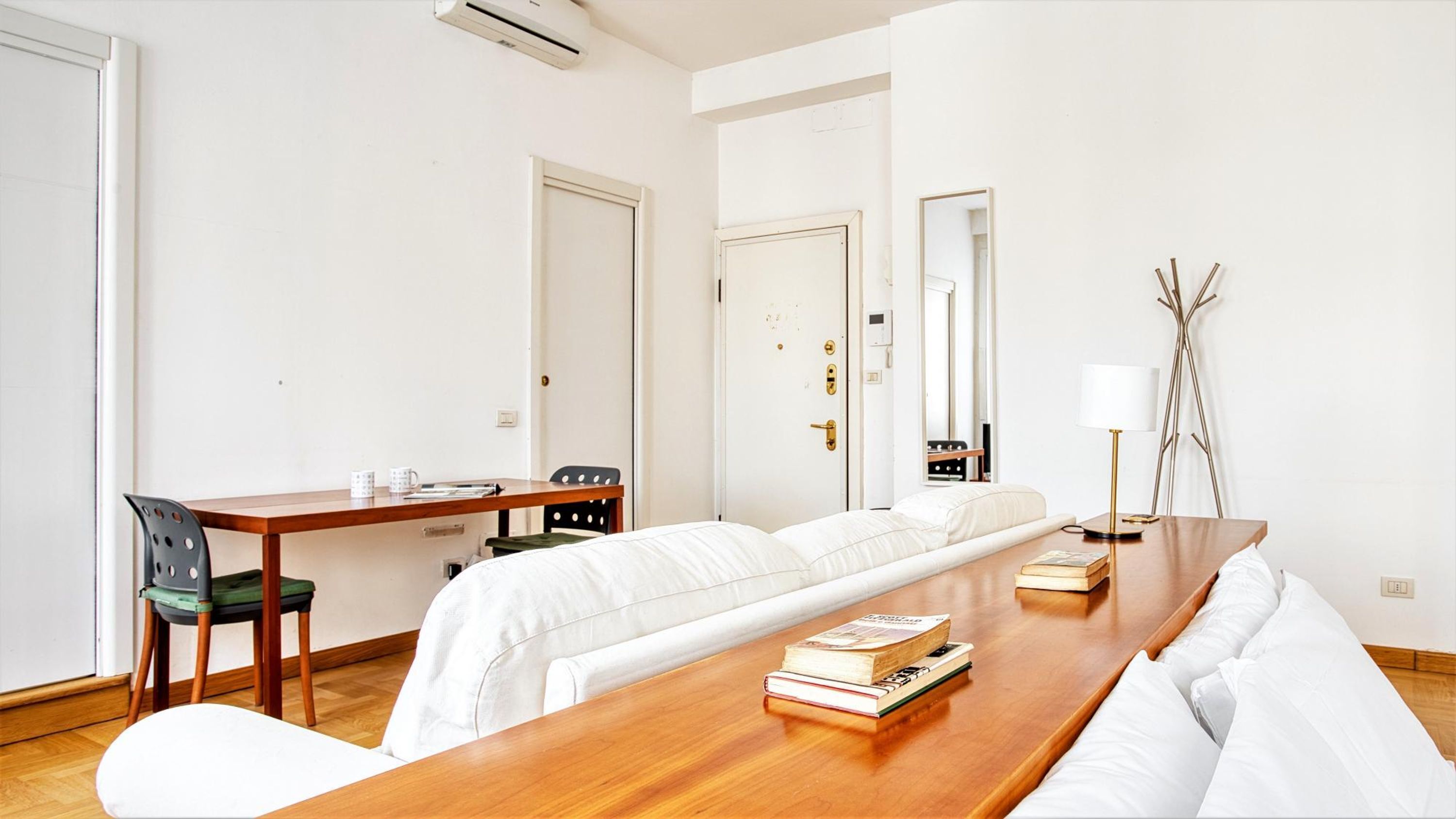 A hotel room with a wooden dining table, a sofa, a chair, a bed, a desk, and a lamp.