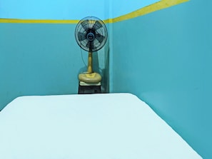 Una habitación con una cama, un ventilador de pie y una pared con una franja amarilla.