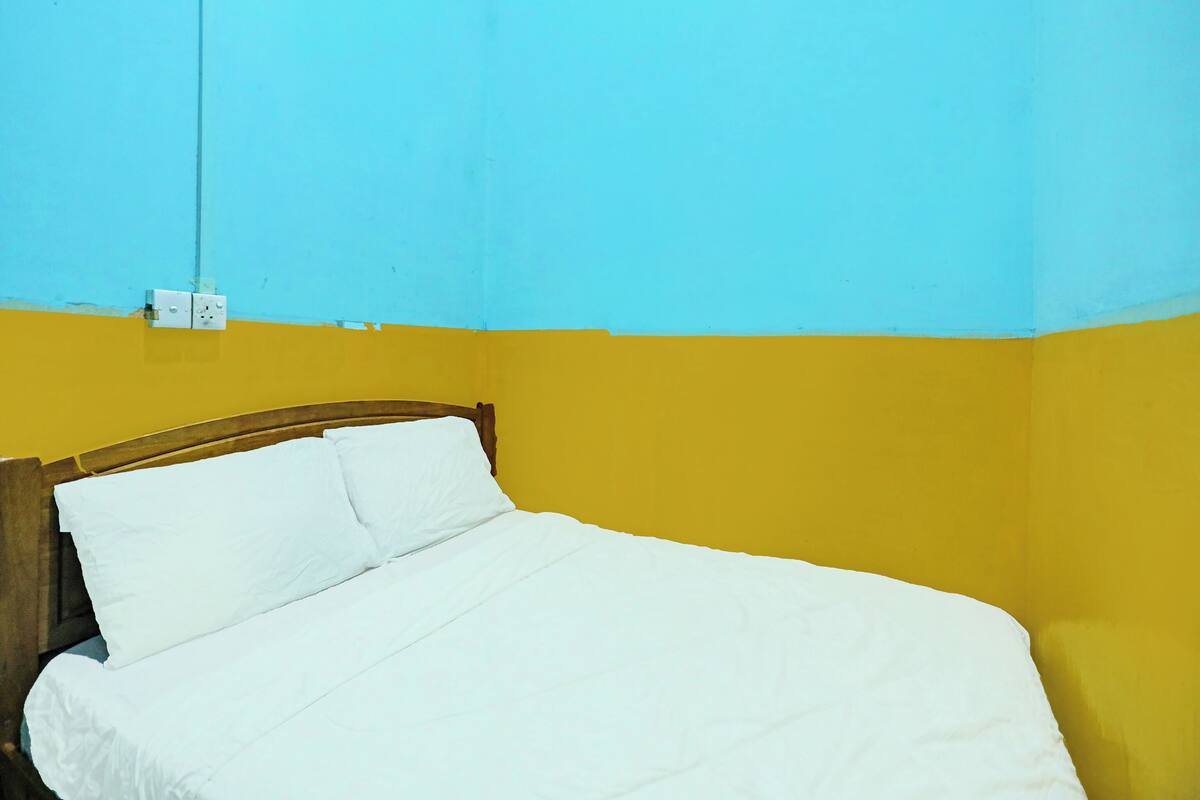 A single bed with white bedding in a room with yellow and blue walls.