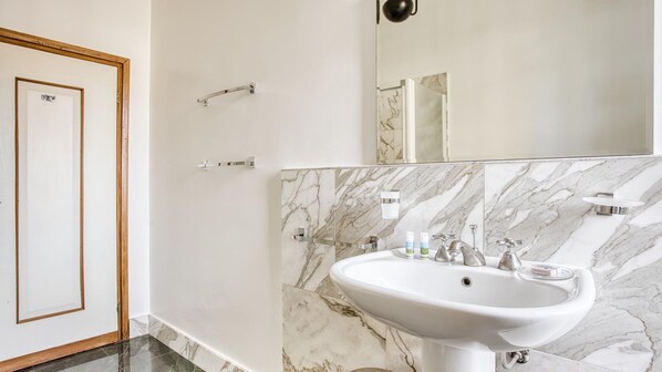 Un baño con pared de azulejos de mármol, un lavabo blanco y un espejo encima.