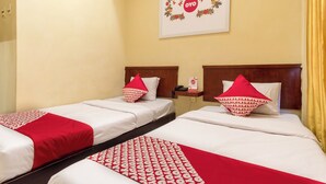 Une chambre d’hôtel avec deux lits, chacun recouvert d’une couvre-lit à motifs rouges et blancs, doté d’une tête de lit en bois et agrémenté d’un oreiller rouge.