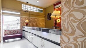 Un hall d’hôtel comprenant un comptoir d’accueil, un banc, un papier peint à motifs et une fenêtre donnant sur les bâtiments environnants.