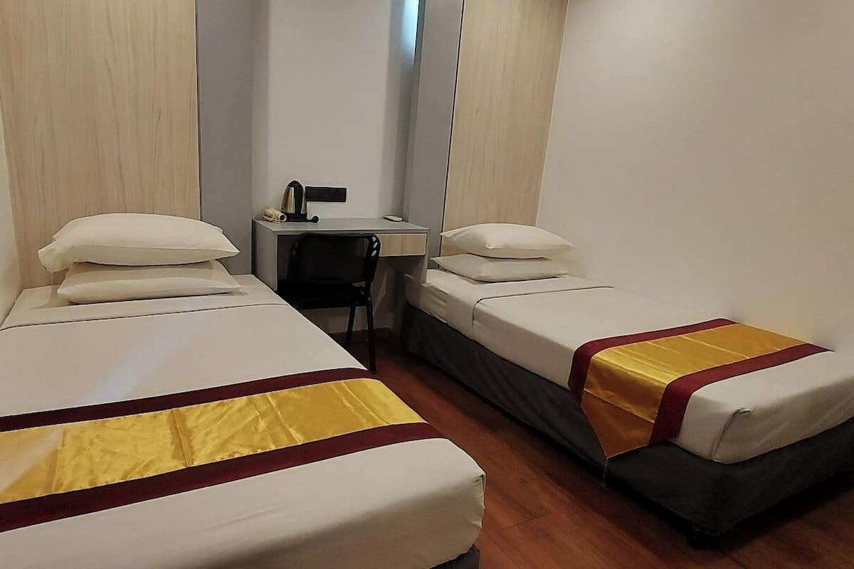 A narrow hotel room with two single beds, each with a pillow and a bedside table.