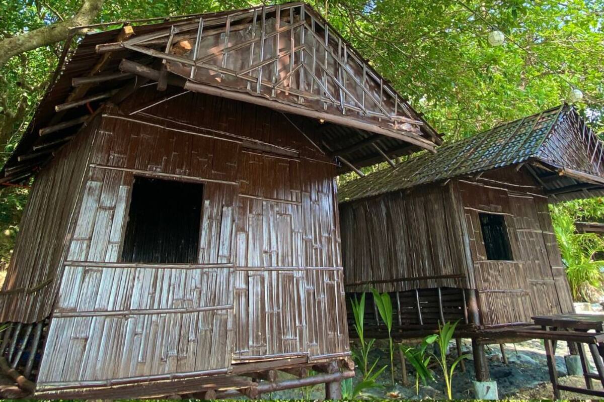 Two rustic wooden structures with steep roofs, surrounded by lush greenery.