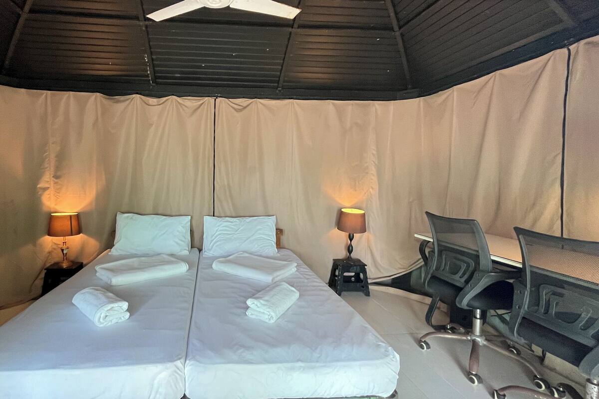 A double bed with white linens, two bedside lamps, a desk with a chair, and a ceiling fan.