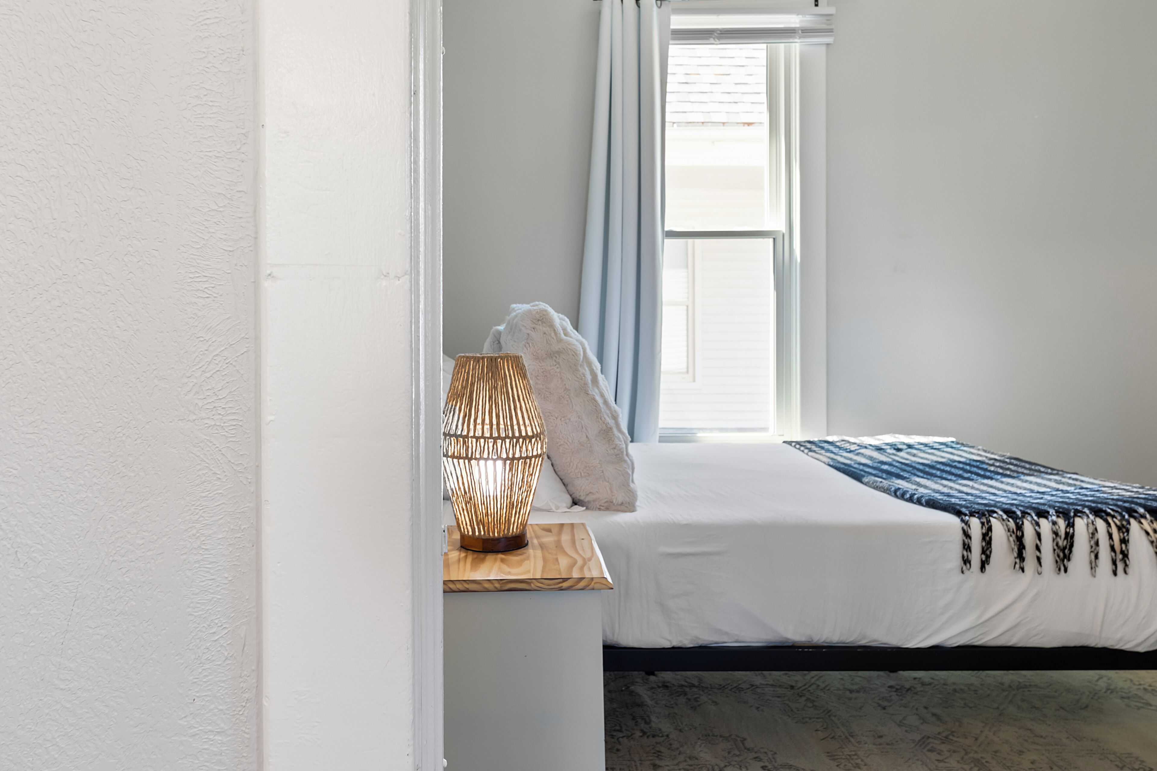 A bedroom with a bed, a bedside lamp, a window with curtains, and a view of the outside.