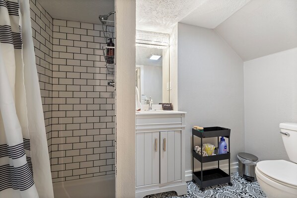 A bathroom with a white sink, a mirror, a toilet, and a shower area with a black and white patterned floor. - Stylish, comfortable centrally located home! TVs in every room, cable (Omaha)