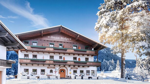 A traditional Alpine Pension building with a wooden facade, multiple balconies, and a snow-covered landscape. - Rustic Tyrolean guesthouse, only 300m from the ski lift (Scheffau am Wilden Kaiser)