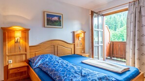 A bedroom with a wooden bed, two bedside lamps, a window with a view of greenery, and a framed picture on the wall. - Rustic Tyrolean guesthouse, only 300m from the ski lift (Scheffau am Wilden Kaiser)