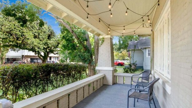 A covered patio with string lights, a concrete bench, and a view of a residential area with trees and parked cars. - Charming Midtown Apt - Hannon Hideaway Unit C (Mobile)