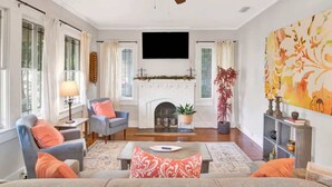 A living room with a fireplace, a ceiling fan, and a large painting. - Charming Midtown Apt - Hannon Hideaway Unit C (Mobile)