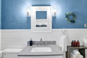 A bathroom with a blue wall, a white sink, a mirror, and a towel rack. - Charming Midtown Apt - Hannon Hideaway Unit C (Mobile)