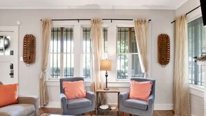 A living room with two armchairs, a coffee table, and a lamp. There are windows with curtains and wall art. - Charming Midtown Apt - Hannon Hideaway Unit C (Mobile)