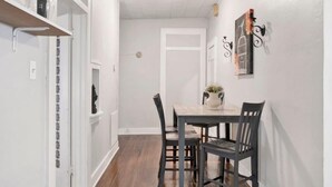 A narrow hallway with a dining area featuring a table and chairs, a white door, and a wall-mounted light fixture. - Charming Midtown Apt - Hannon Hideaway Unit C (Mobile)
