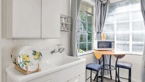 A compact kitchen with a white sink, a microwave, and a small table with two chairs. - Charming Midtown Apt - Hannon Hideaway Unit A (Mobile)