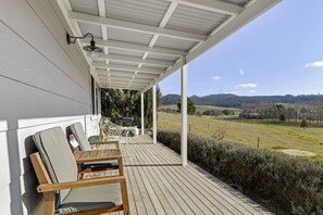 A covered porch with wooden chairs and a table, overlooking a scenic landscape with hills and a clear sky. - Towac Cabin 1 • Mt Canobolas Views • Orange (Canobolas)
