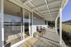 Un espacio al aire libre cubierto con terraza de madera, puertas corredizas de vidrio y mobiliario exterior.