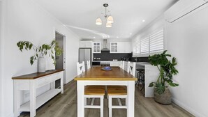 A modern kitchen with white cabinetry, a wooden dining table, and pendant lighting.