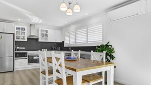 A modern kitchen with white cabinetry, a wooden dining table, and a built-in oven.