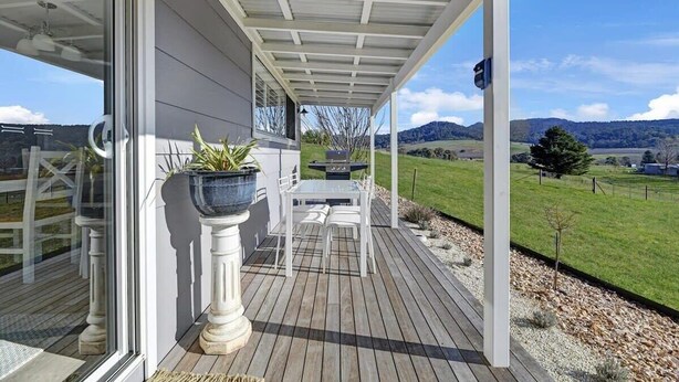 A covered outdoor patio with a table and chairs, potted plants, and a view of a green landscape.