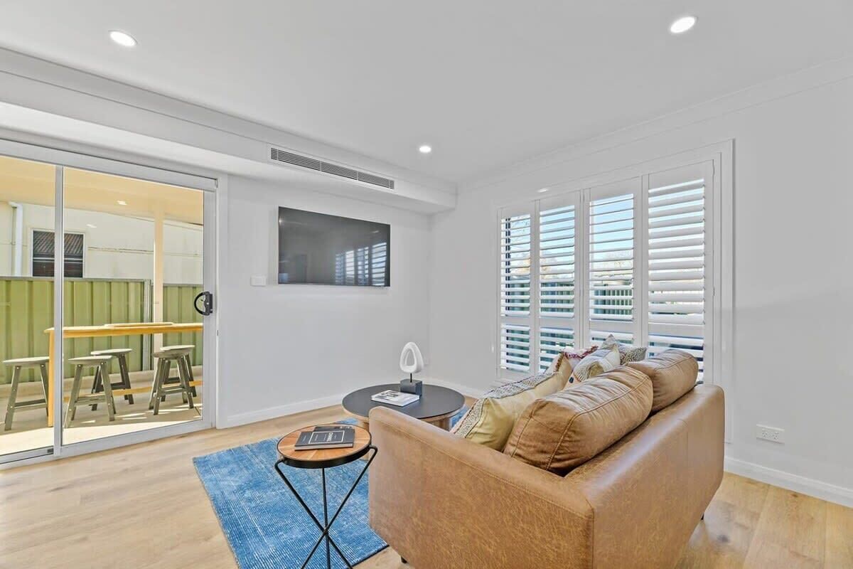 A modern living room with a sofa, a coffee table, and a dining area visible through glass doors.