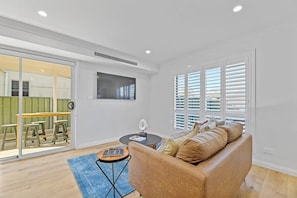 A modern living room with a sofa, a coffee table, and a dining area visible through glass doors. - Cosy on Curran | CBD Escape, EV Plug, Firepit (Orange)