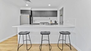 Une cuisine moderne dotée d’un îlot central, de trois tabourets et d’une cuisinière intégrée.
