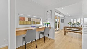 Une cuisine moderne avec un plan de travail en bois, deux chaises grises, une table à manger en bois avec des bancs, et une fenêtre avec des stores.