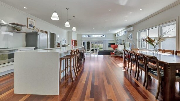 A spacious kitchen with a central island, wooden flooring, pendant lighting, and a view to the dining area.