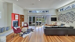 A spacious living room with a fireplace, a red accent wall, a large black sofa, and a wall of framed photos.