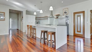 A modern kitchen with a central island, wooden bar stools, pendant lighting, and a stainless steel range hood.