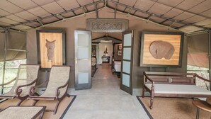 Un pasillo con techo alto, bancos de madera y una puerta central abierta que da a una habitación con cama y candelabro.