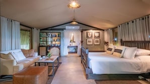 Una habitación acogedora con cama, sofá y una mesita. Se aprecia una estantería y una ventana con cortinas.