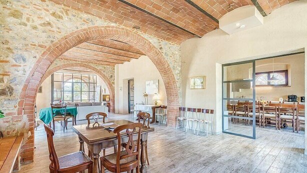 A spacious dining area with a rustic brick archway, wooden tables, and chairs.