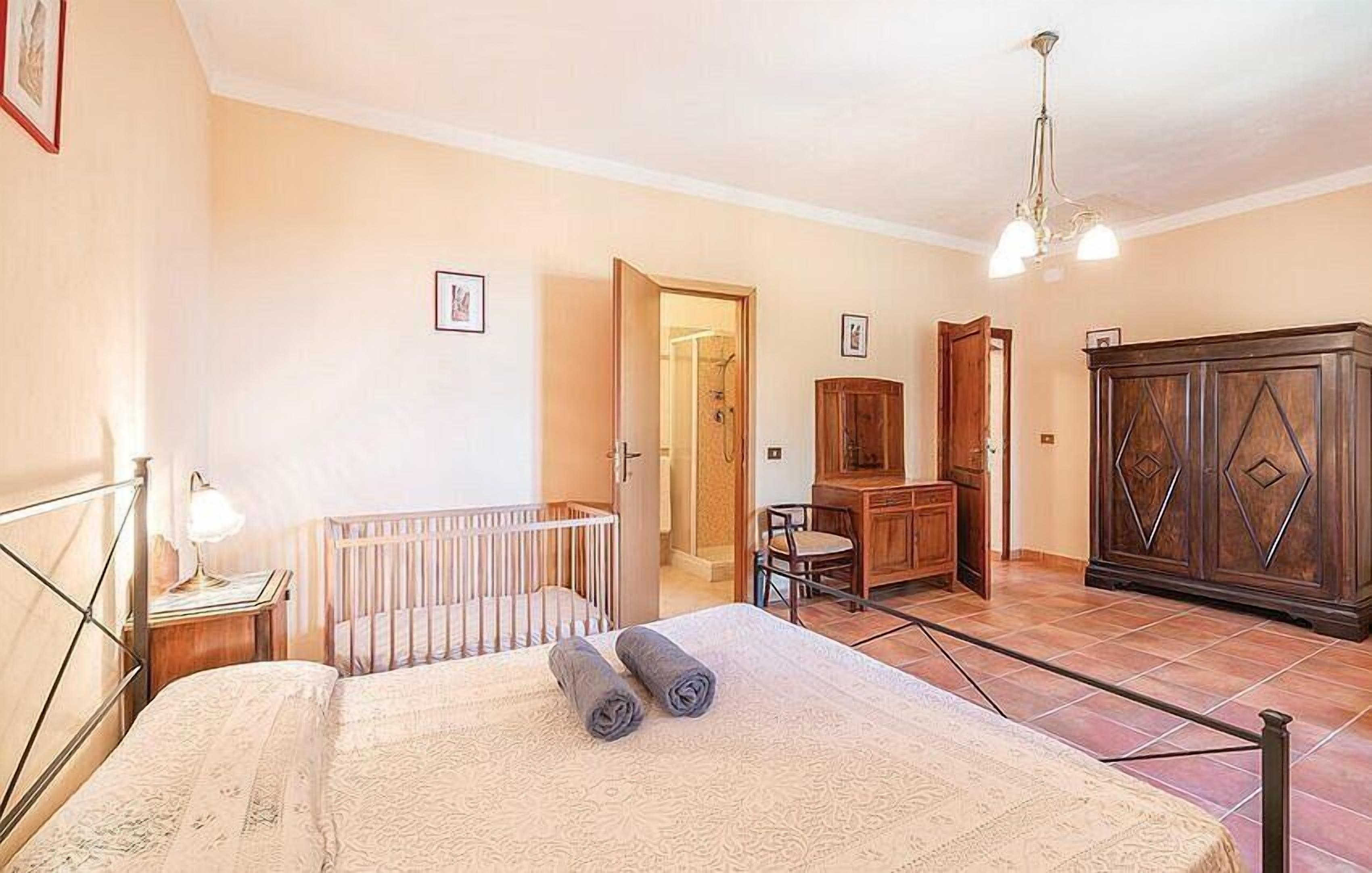 A bedroom with a bed, a crib, a wooden wardrobe, and a desk with a chair.