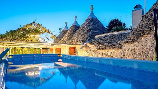 A swimming pool with stone-roofed buildings in the background. - Trullo Resia: A cozy and welcoming trullo in the characteristic style of the Apulian countryside, with Free WI-FI. (Ostuni)