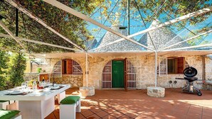 An outdoor patio with a stone wall, a grill, and a table set for dining. - Trullo Resia: A cozy and welcoming trullo in the characteristic style of the Apulian countryside, with Free WI-FI. (Ostuni)