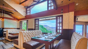 A dining area with a high table set for six, surrounded by leather sofas and wooden benches. Large windows offer a view of a mountainous landscape. - Pax Ark Dalhousie (Dalhousie)