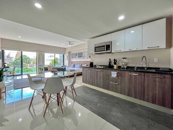 A modern kitchen with a dining area, large windows, and a view of the city.
