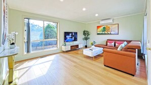 A spacious living room with a large window, a flat-screen TV, a sofa, and a coffee table. - Ringwood 2BR Home  (Ringwood)
