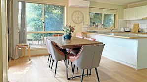 A modern kitchen with a dining area, large windows, and a view of greenery. - Ringwood 2BR Home  (Ringwood)