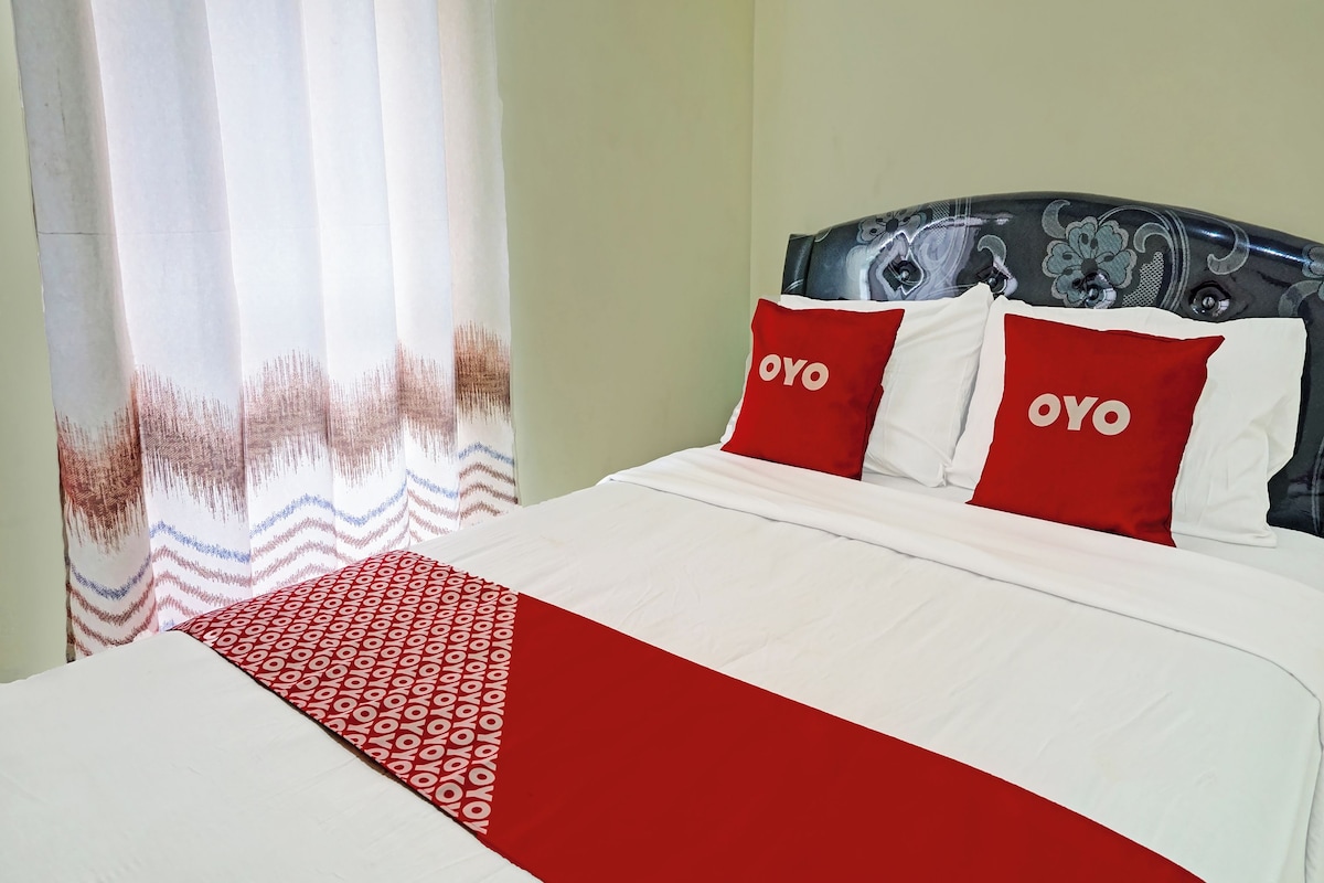 A bed with white and red bedding, two pillows with 'OYO' text, and a patterned throw.